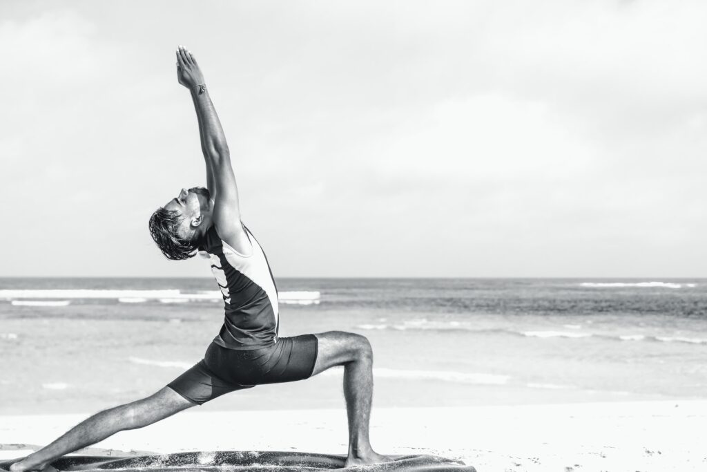 A senior woman in crescent moon pose, with one leg bent and the other extended behind her, and her arms extended to the sides.