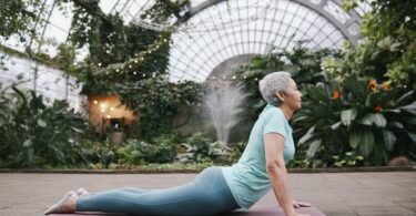 An image of a senior woman practicing yoga in a chair: "Senior woman in yoga for seniors chair class, sitting and holding onto chair for support while doing yoga poses"