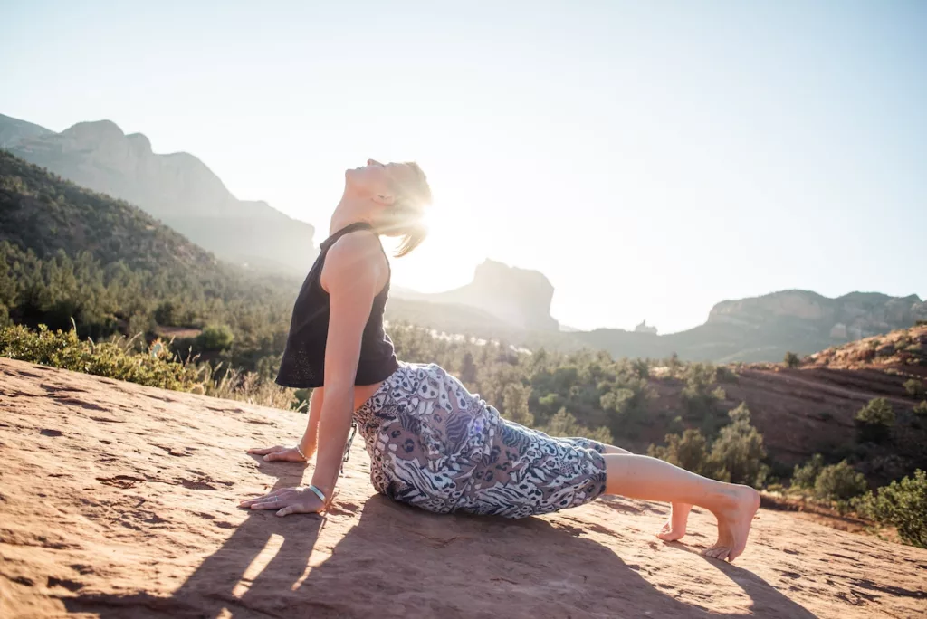 Woman doing Bhujangasana on sunlit cliff
